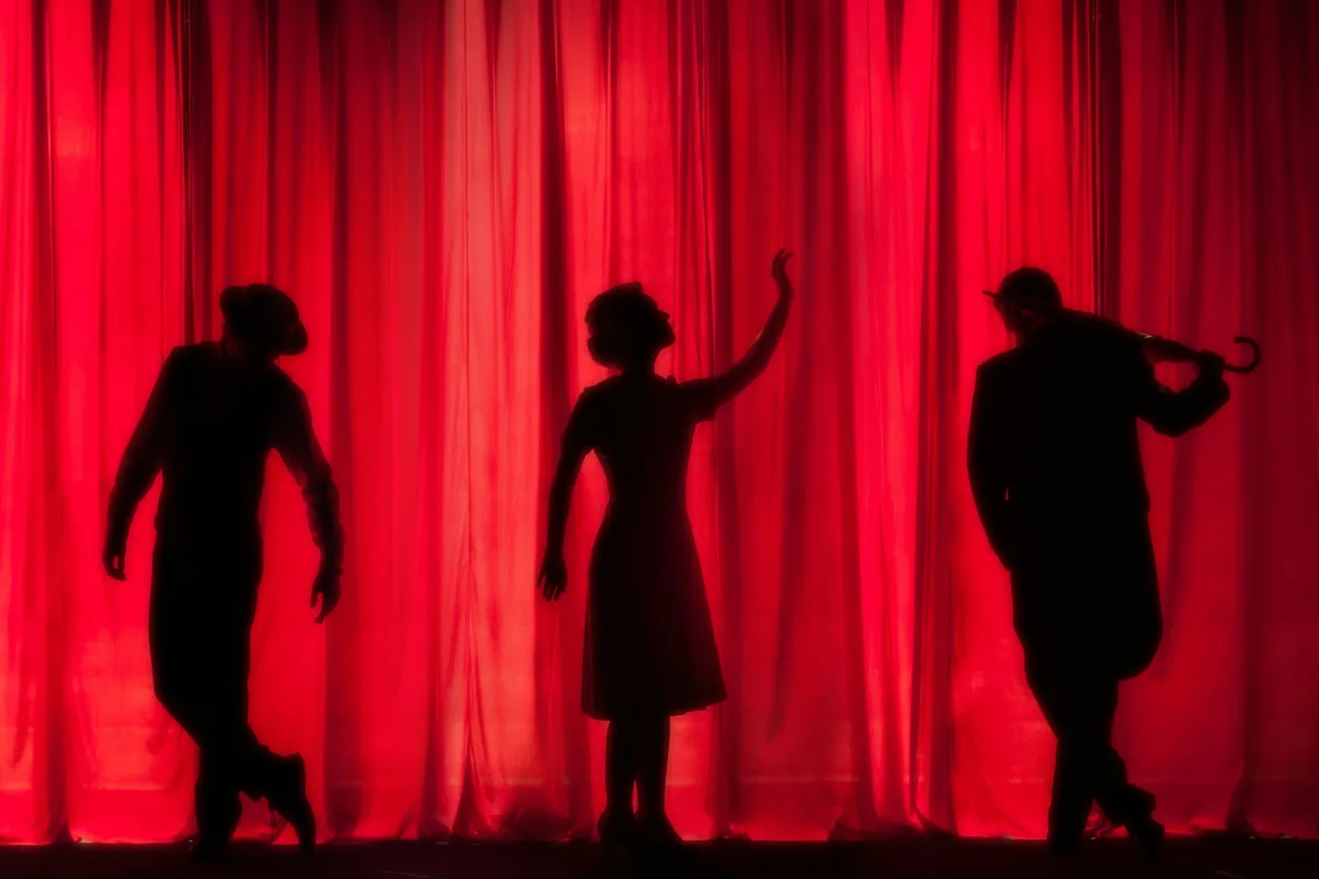 Three silhouetted performers against a lit red curtain