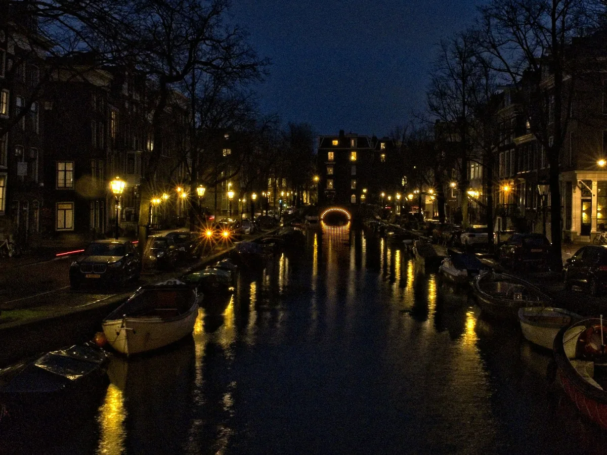 An Amsterdam canal at night, boats moored along both banks, windows lit